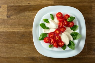 Ahşap bir masada fesleğen ve kiraz domatesli Mozzarella. Kopyalama alanı olan üst görünüm.