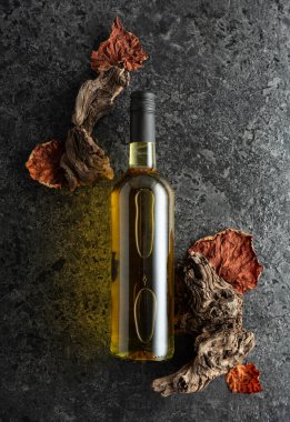 Siyah taşlı arka planda bir şişe beyaz şarap. Beyaz şarap, eski pürüzler ve kurumuş asma yaprakları. Üst Manzara. Boşluğu kopyala.