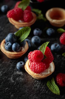 Siyah arka planda naneli taze ahududu ve yaban mersinli küçük tartlar..