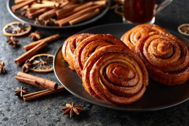 Kanelbullar - İsveç tarçınlı çörekler ya da dürümler. Siyah taş bir masada taze pişmiş çörekler..