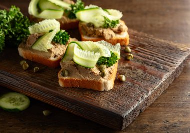 Eski bir kesme tahtasında ezmeli tost. Taze salatalık, kapari ve maydanozlu açık ezmeli sandviçlerle dolu bir hayat..
