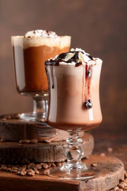 Kahverengi arka planda krem şantili ve çikolata soslu çikolata içecekleri..