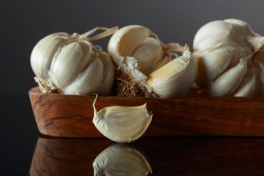 Siyah yansıtıcı arka planda ahşap kaptaki sarımsak soğanları. Boşluğu kopyala.