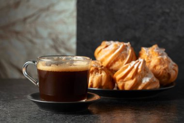 Cam bardakta sade kahve ve siyah taş masada kremalı kek. Boşluğu kopyala.