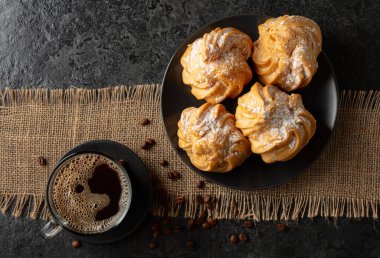 Kremalı kek ve sade kahve siyah taş bir masada. Üst görünüm.