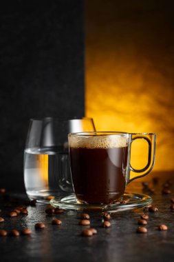 Espresso, bir bardak soğuk su ve siyah taş bir masada kavrulmuş kahve çekirdekleri. Boşluğu kopyala.