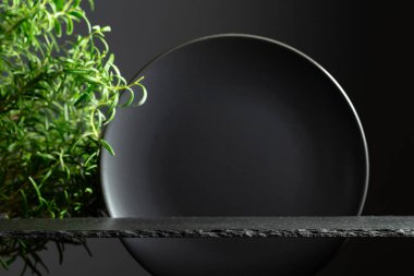 Siyah taş podyum, siyah seramik plaka ve lüks ürün yerleştirme için biberiye dalları. Minimum lüks estetik. Boşluğu kopyala.