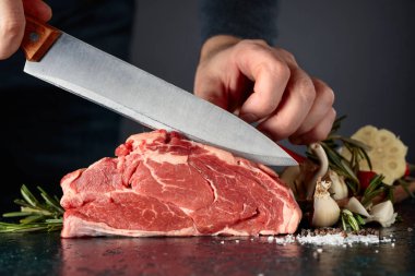 Şef çiğ et kesiyor. Biberiye, sarımsak, tuz ve biberli bir masada.