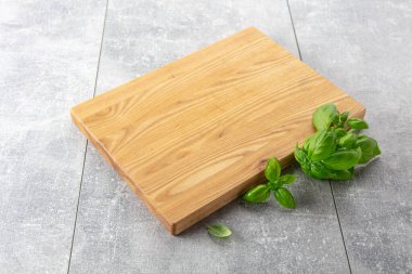 Gri bir mutfak masasında fesleğen ve tahta kesmek. Mutfak geçmişi. Boş tahta kesme tahtası, ürün görüntüleme alanı.