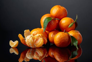 Tangerines or clementines with green leaves on a black reflective background. Copy space.