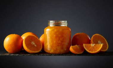 Cam kavanozda portakal reçeli ve taze meyve. Siyah arka planda güzel bir kesişme. Boşluğu kopyala.