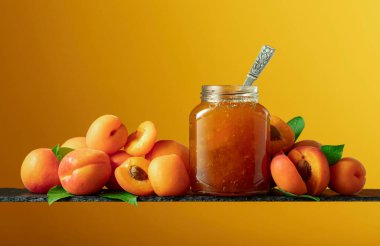 Cam kavanozda kayısı reçeli ve taze meyve. Turuncu arka planda tatlı bir kesişme. Boşluğu kopyala.