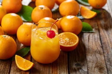 Kırmızı kirazla süslenmiş buzlu portakal suyu. İçki ve taze meyveler eski ahşap bir masada.