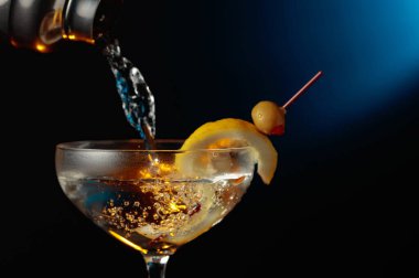 Yeşil zeytinli ve limonlu martini. Kokteyl bardaktan bardağa dökülüyor..