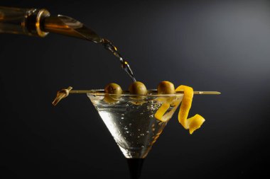 Siyah arka planda yeşil zeytinli ve limon kabuklu klasik sek martini kokteyli. Metnin için boş yer.