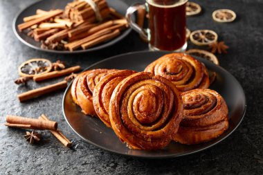 Kanelbullar - İsveç tarçınlı çörekler ya da dürümler. Siyah taş bir masada taze pişmiş çörekler..