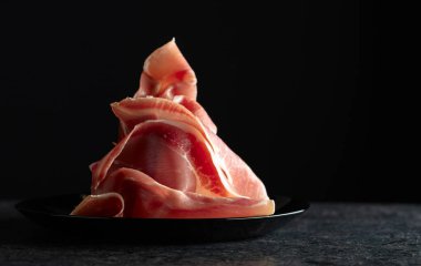 İtalyan jambon kabuğu, siyah arka planda dilimlenmiş ham jambon bacağı. Boşluğu kopyala.