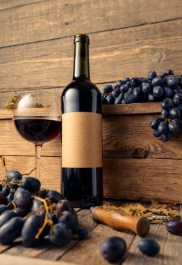 Eski ahşap bir masada bir şişe kırmızı şarap ve mavi üzüm. Eski boş bir şişede. Boşluğu kopyala.