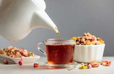 Bitki çayı cam bardağa dökülür. Kurutulmuş ot ve çiçek karışımları taş masaya saçıldı. Boşluğu kopyala.