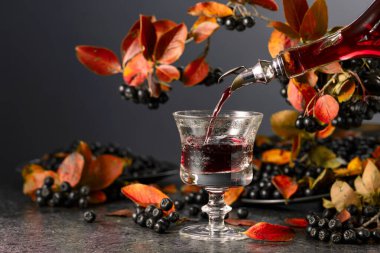 Böğürtlen suyu şişeden bardağa dökülür. Tatlı içecek ve taze böğürtlen siyah bir taş masada..