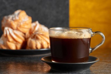 Cam bardakta sade kahve ve siyah taş masada kremalı kek. Boşluğu kopyala.