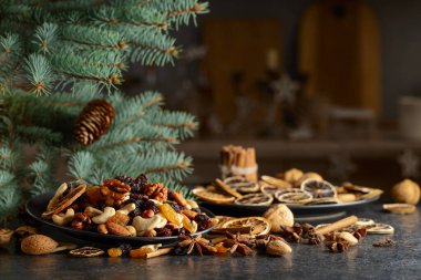 Noel baharatları, çeşitli fındıklar, kuru üzümler ve mutfak masasındaki kuru narenciye dilimleri. Noel 'de ladin dalları ve kurumuş meyvelerle dolu sakin bir hayat. Boşluğu kopyala.