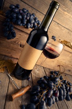 Eski ahşap bir masada bir şişe kırmızı şarap ve mavi üzüm. Eski boş bir şişede. Boşluğu kopyala.