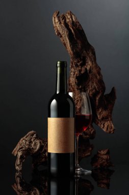 Eski, boş etiketli bir şişe kırmızı şarap. Arka planda eski yıpranmış bir pürüz var. Siyah yansıtıcı arka plan. Metnin için alanı olan ön görünüm.