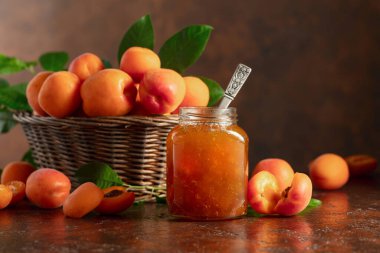Cam kavanozda kayısı reçeli ve kahverengi bir masada taze meyve. Boşluğu kopyala.