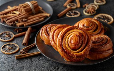 Kanelbullar - İsveç tarçınlı çörekler ya da dürümler. Siyah taş bir masada taze pişmiş çörekler..