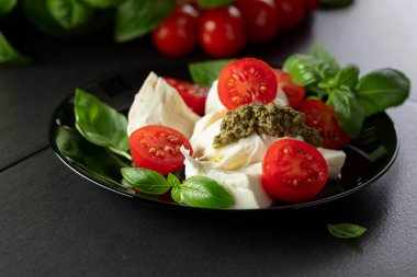 Fesleğenli Mozzarella, vişneli domates ve siyah tabakta pesto sosu. Geleneksel İtalyan mutfağı.
