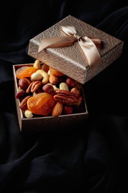 Kurutulmuş meyve ve fındık siyah bir kumaş üzerinde hediye kutusunda..