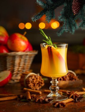 Elma dilimli sıcak şarap, tarçın, biberiye ve anason. Geleneksel sıcak bayram içeceği. Arka planda mutfak aletleri ve yanan mumlar..