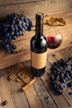 Eski ahşap bir masada bir şişe kırmızı şarap ve mavi üzüm. Eski boş bir şişede. Boşluğu kopyala.