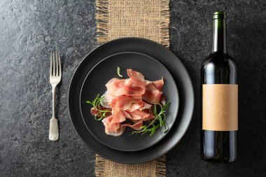 Bir şişe kırmızı şarap ve siyah tabakta jambon. Boş bir şişede. Üst görünüm.