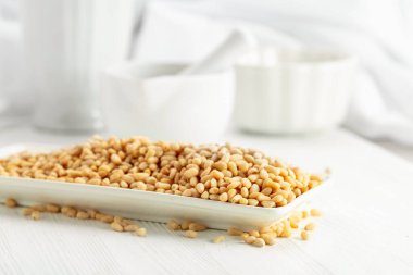 Beyaz ahşap bir masada soyulmuş çam fıstığı. Beyaz arka planda beyaz tabakta çam fıstığı.