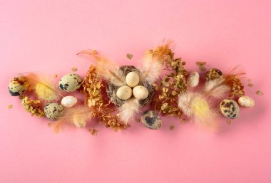 Paskalya kompozisyonu bıldırcın yumurtaları, tüyler ve pembe arka planda kurumuş çiçekler. Üst görünüm.