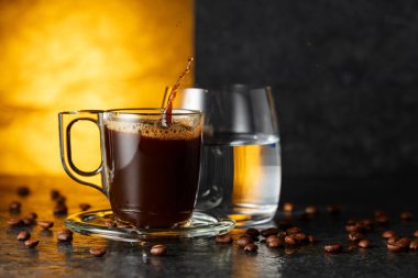 Espresso, bir bardak soğuk su ve siyah taş bir masada kavrulmuş kahve çekirdekleri. Boşluğu kopyala.