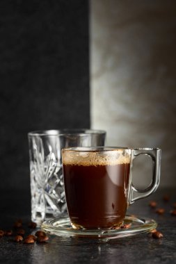 Espresso, bir bardak soğuk su ve arka planda kavrulmuş kahve çekirdekleri. Boşluğu kopyala.