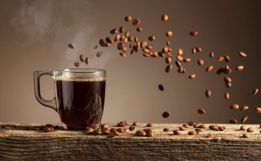 Eski ahşap bir masada cam bardakta espresso. Kavrulmuş kahve çekirdekleri hareket halinde. Boşluğu kopyala.