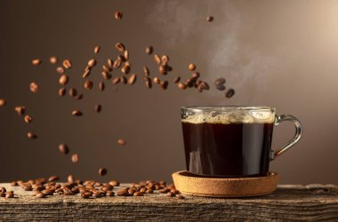 Eski bir tahtanın üzerinde cam bardakta sade kahve. Kavrulmuş kahve çekirdekleri hareket halinde. Boşluğu kopyala.