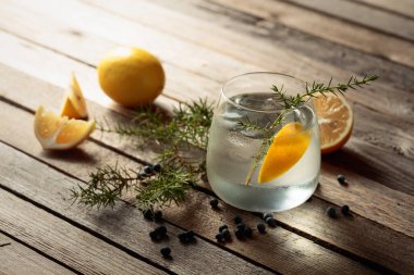 Limonlu alkol içeceği (cin tonik kokteyli), ardıç dalı ve kırsal ahşap masa üzerindeki buz, kopyalama alanı. Limon ve ardıç meyveli buzlu kokteyl..