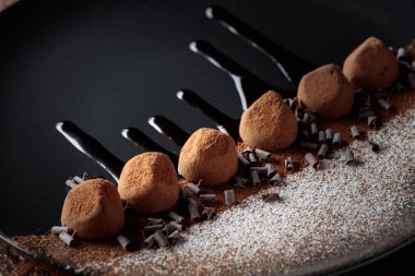 Çikolatalı trüf mantarı, siyah tabakta, çikolata soslu. Tatlılar kakao tozu ve pudra şekeriyle serpiştirilir..