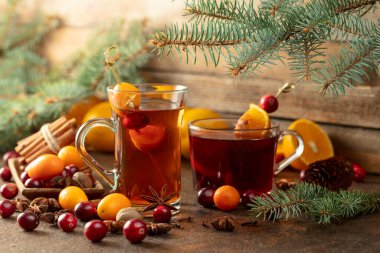 Eski bir mutfak masasında malzemelerle kış içkileri. Masaya dağılmış yabanmersini, kumkat, portakal, anason, tarçın, hindistan cevizi ve karanfil var..