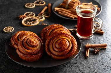 Kanelbullar - İsveç tarçınlı çörekler ya da dürümler. Siyah taş bir masada taze pişmiş çörekler..