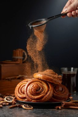 Kanelbullar - İsveç çörekleri ya da ekmekler üzerine tarçın serpiştirilmiş. Siyah arka planda taze pişmiş çörekler..