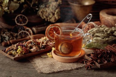 Bir fincan bitkisel çay, çeşitli kurutulmuş bitkiler, çiçekler ve baharatlar. İçindekilerle çay ve kurutulmuş portakal dilimleri..