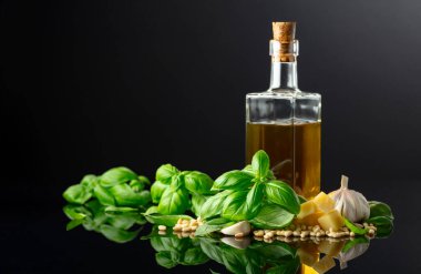 Pesto sosu yapmak için gerekli malzemeler. Fesleğen, çam fıstığı, sarımsak, parmesan ve siyah yansıtıcı arka planda zeytin yağı. Geleneksel İtalyan pesto tarifi.