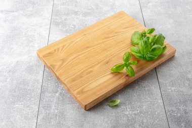 Gri bir mutfak masasında fesleğen ve tahta kesmek. Mutfak geçmişi. Boş tahta kesme tahtası, ürün görüntüleme alanı.