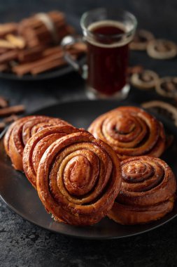 Kanelbullar - İsveç tarçınlı çörekler ya da dürümler. Siyah taş bir masada taze pişmiş çörekler..